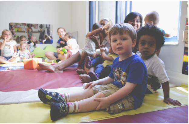 A group of children and parents sit on a colorful mat in the EarlyON program